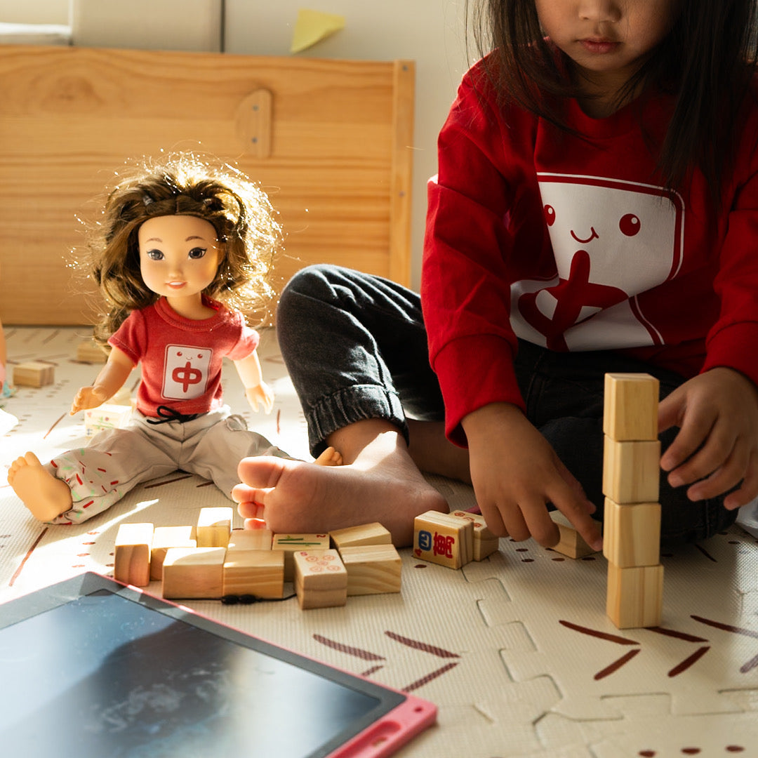 Child playing with wooden mahjong blocks and an asian american doll on a patterned floor.