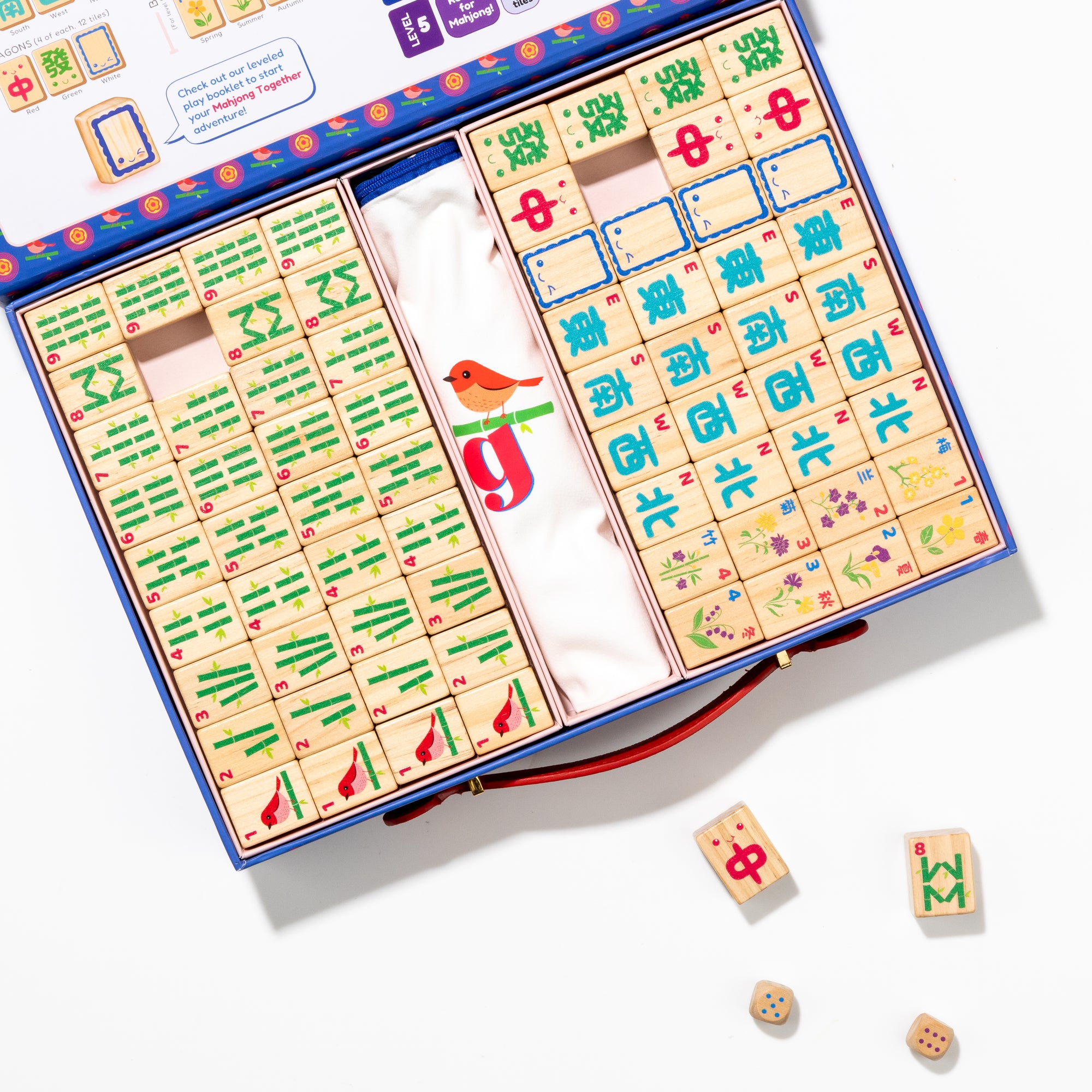 Open children's mahjong set with tiles and dice on a white background