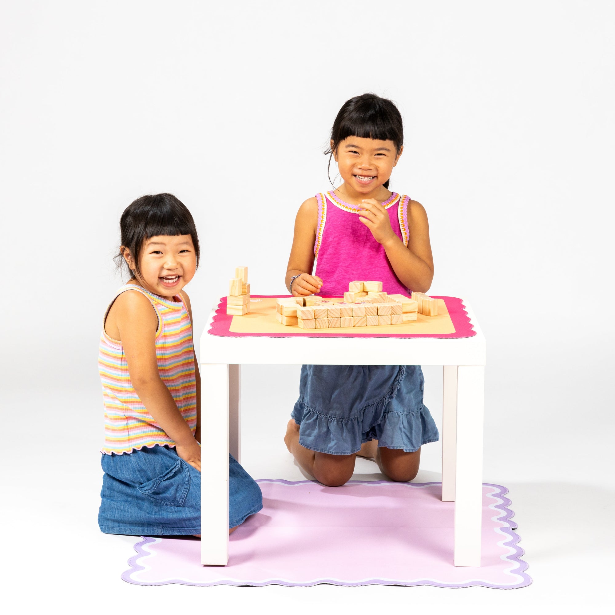Two young girls playing with building Mahjong on a small table against a white background