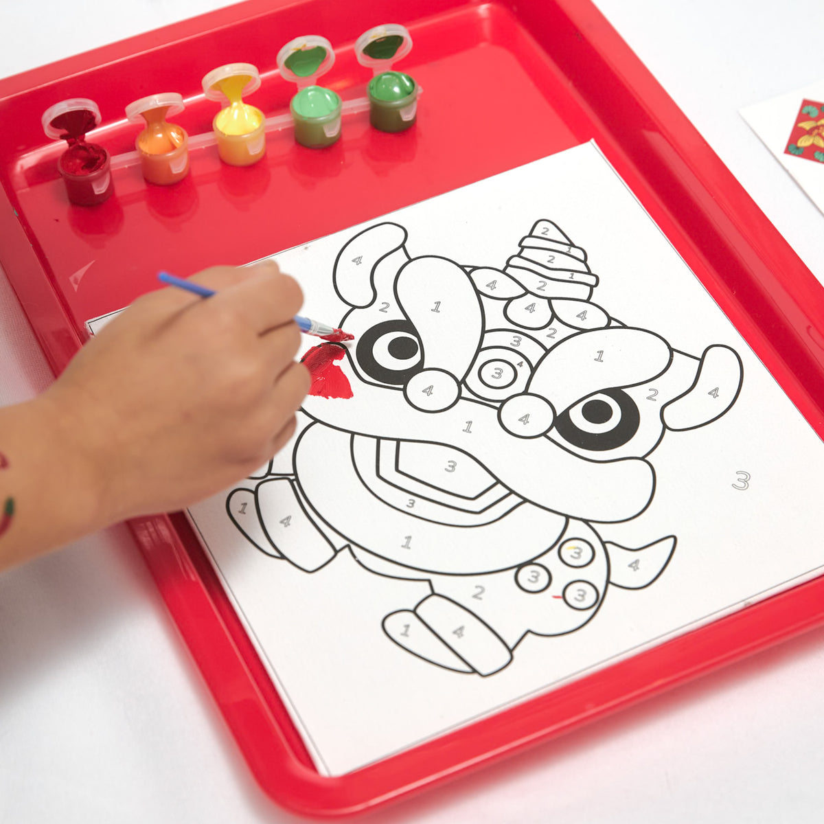 Paint-by-number kit featuring Lunar New Year symbols—fish, oranges, and a lion dance—with canvases, paints, and brushes for creative fun.